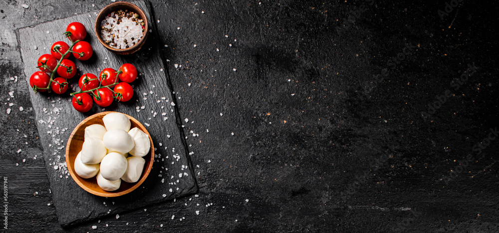 Mozzarella cheese in a plate on a stone board with tomatoes and spices. Mozzarella cheese in a plate on a stone board with tomatoes and spices.