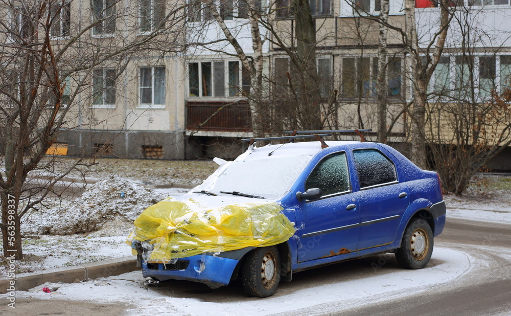 An old blue rusty car is covered with yellow film after an accident, Iskrovsky Prospekt, St. Petersburg, Russia, January 2023