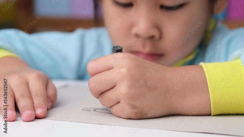 Cheerful happy little girl drawing with crayons on paper sitting at table in her room at home. Creativity and development of fine motor skills.