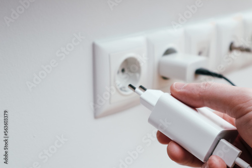 Man hands plugging the charger into an outlet in the wall, close-up. Hand turns on, turns off charger in electrical outlet on wall photo