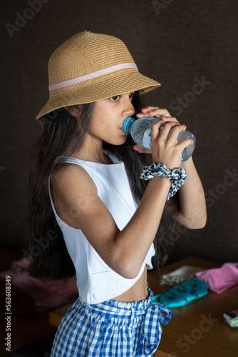 An Asian Indian origin school age girl looks thoughtful and drinks water from a bottle.