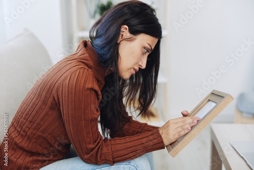 Woman looking sadly at the picture frames in her hands, crying over memories, state of depression and loss of a person