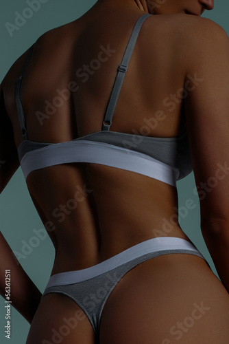 Skinny tanned woman in gray lingerie closeup from back on mint background