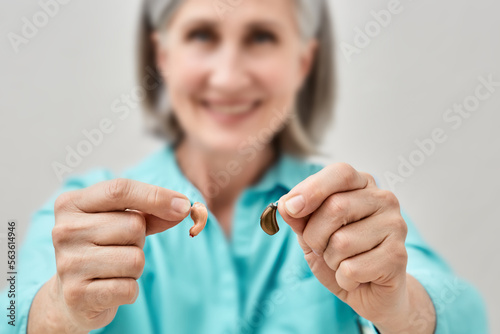 Mature woman with hearing problems chooses between behind-the-ear hearing aid and in-the-ear hearing aid by holding them in front of her. Hearing aids and solutions photo