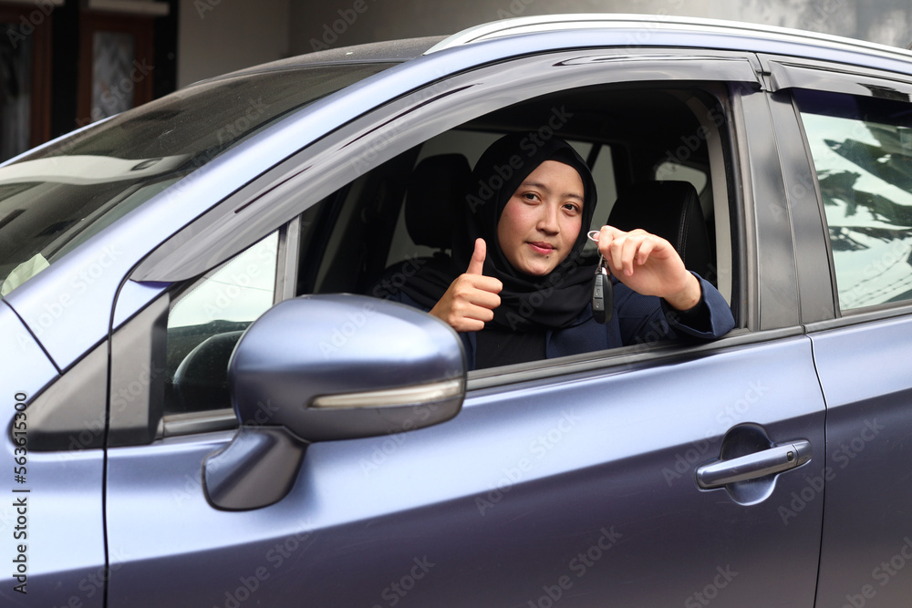 Muslim woman in hijab driving and showing car keys out the window while giving the thumb up.