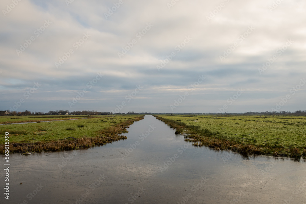 Typical Dutch rural scenery showing the flat Netherlands. canal water is part of a flood management system for the polder which is land reclaimed from the sea and converted into arable farm fields