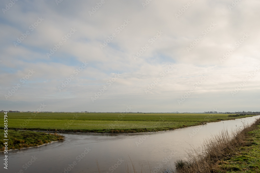 Typical Dutch rural scenery showing the flat Netherlands. canal water is part of a flood management system for the polder which is land reclaimed from the sea and converted into arable farm fields