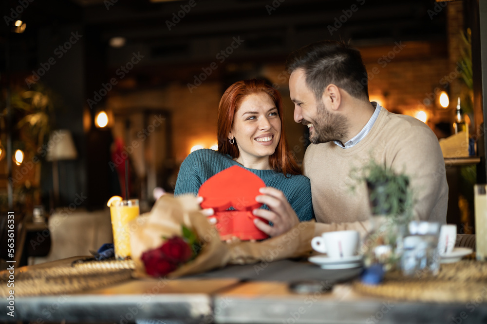 Valentines day couple sitting in favourite caffe, exchanging gifts in hart shape