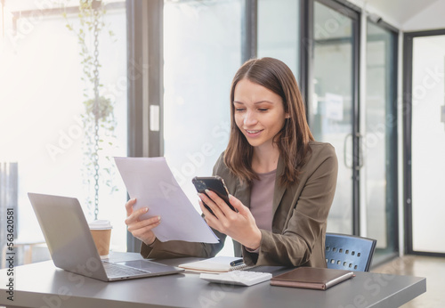 Marketing, Finance, Accounting, Planning, Businesswoman of bi nationality is talking with a customer representing a company distributor using a smartphone with laptop pen and notepad on office desk.