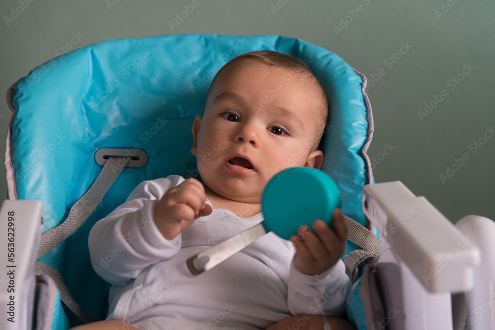 Obraz premium baby in the child chair playing with kitchen utensil