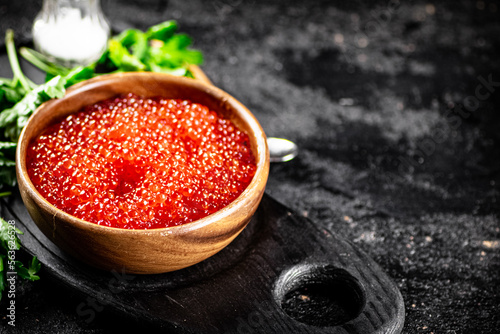 Red caviar in a plate on a cutting board with parsley. 