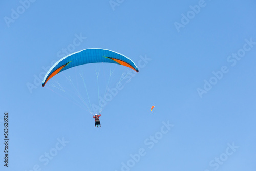 Two paraglider tandem fly against the blue sky, tandem paragliding on distance guided by a pilot.