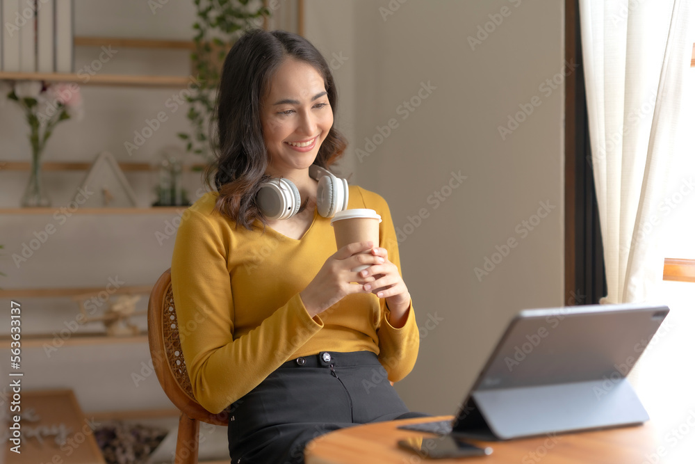 Pretty Asian businesswoman sitting holding coffee at home working smiling and enjoying working with laptop happily. Pretty Asian businesswoman sitting holding coffee at home working smiling and enjoying working with laptop happily.