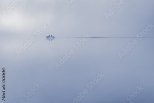 Silhouette of fishermen in a boat on a calm water surface in the early morning at dawn.