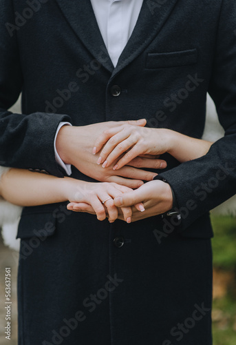 A man in a black cashmere coat and a woman, the bride and groom hold hands close-up. Photography, closeup portrait, idea, concept, wedding, copy space.