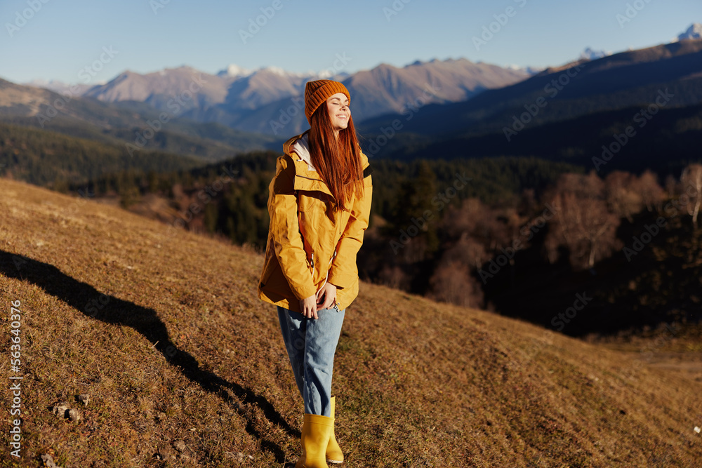 Woman smile with teeth full-length walk happiness walking on the hill and looking at mountains in a yellow raincoat and jeans in the autumn happy journey in the sun sunset hiking, freedom lifestyle 