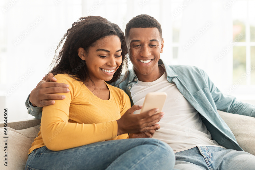 Glad young african american guy and woman look at phone, have video call, watch video Glad young african american guy and woman look at phone, have video call, watch video