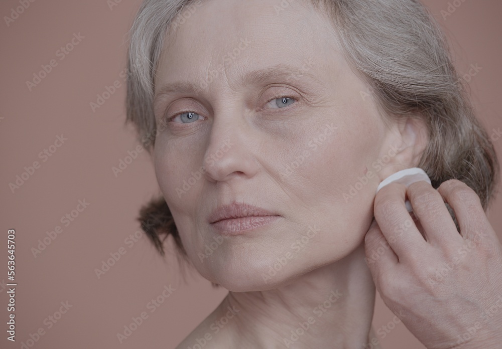 CU Portrait of very beautiful grey-haired 60s mature senior adult female doing her skincare routine. Studio shot, soft lighting. No make up, clean skin CU Portrait of very beautiful grey-haired 60s mature senior adult female doing her skincare routine. Studio shot, soft lighting. No make up, clean skin