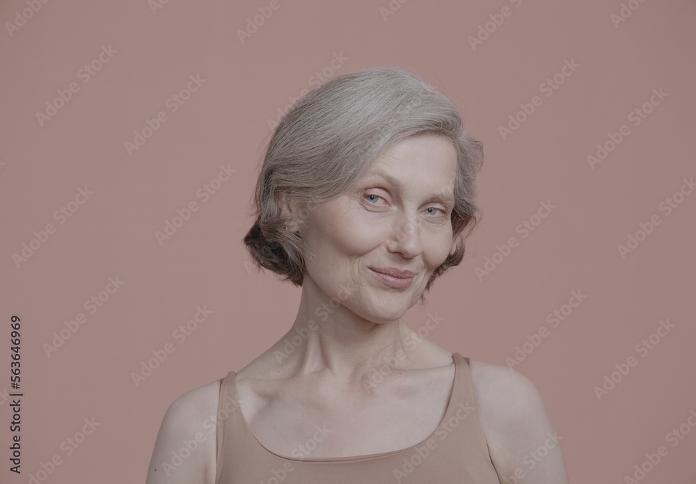CU Portrait of beautiful 60s grey-haired mature senior adult female posing without makeup against light brown background. Studio shot, soft lighting. No make up, clean skin CU Portrait of beautiful 60s grey-haired mature senior adult female posing without makeup against light brown background. Studio shot, soft lighting. No make up, clean skin