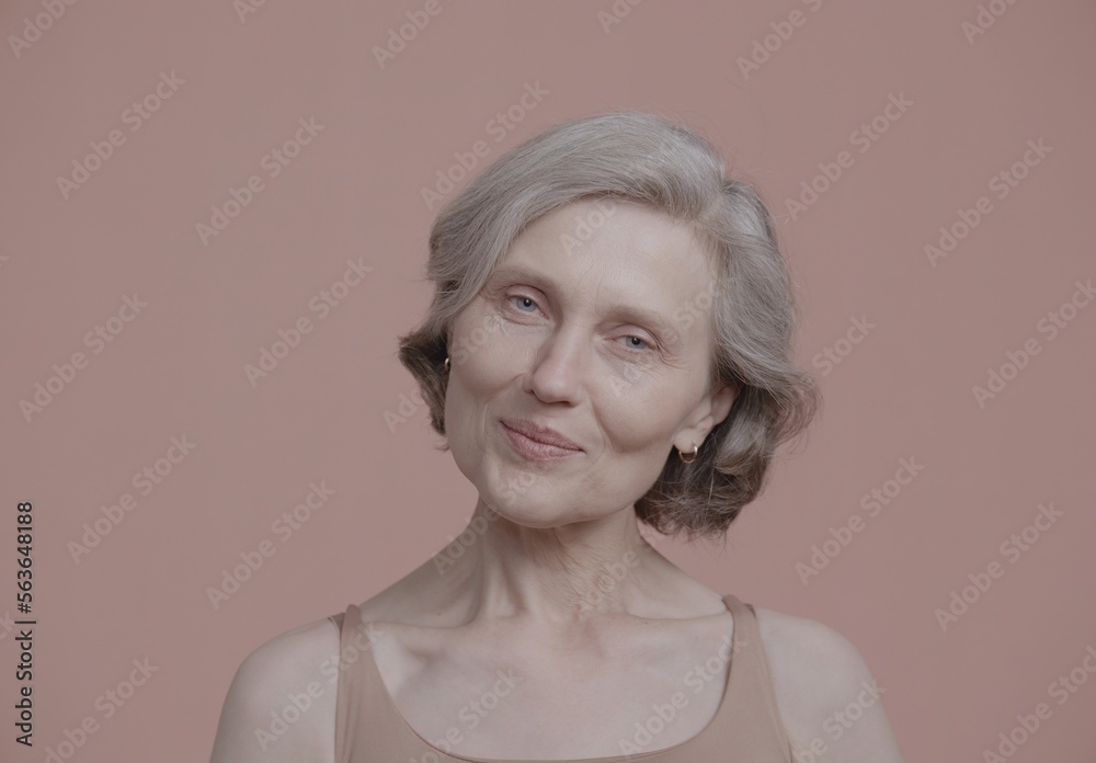 CU Portrait of beautiful 60s grey-haired mature senior adult female posing without makeup against light brown background. Studio shot, soft lighting. No make up, clean skin