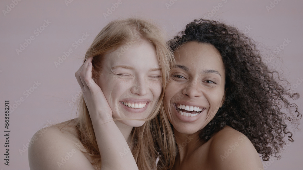 Fototapeta premium Candid portrait of two beautiful 20s females, African-American Black and Caucasian, posing against solid background, no make-up, studio shot, soft lighting