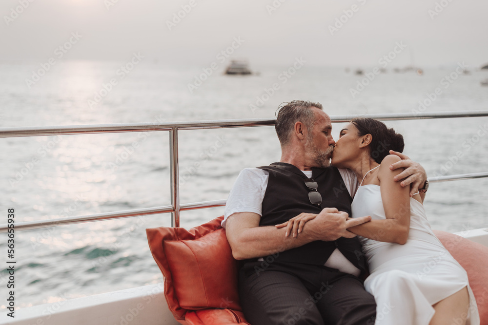 Romantic couple love kissing on yacht. Happy man and woman sitting on side of boat and hugging in cruise ship while sunset on vacation. luxury and honeymoon lifestyle, happy anniversary.