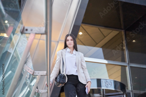 Beautiful female entrepreneur standing outdoors with smartphone in hands, leaving office, businesswoman in dressed in formal clothes waiting for taxi