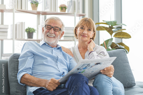 Happy husband and wife senior couple elderly family, caucasians mature, adult lover and retired man, woman reading newspaper, report on sofa together at home. Husband and wife lifestyle.