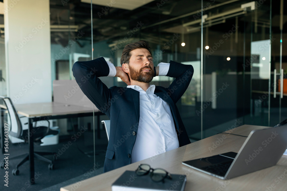 Relaxed male entrepreneur resting with closed eyes at workplace in office, leaning back in chair with hands behind head Relaxed male entrepreneur resting with closed eyes at workplace in office, leaning back in chair with hands behind head