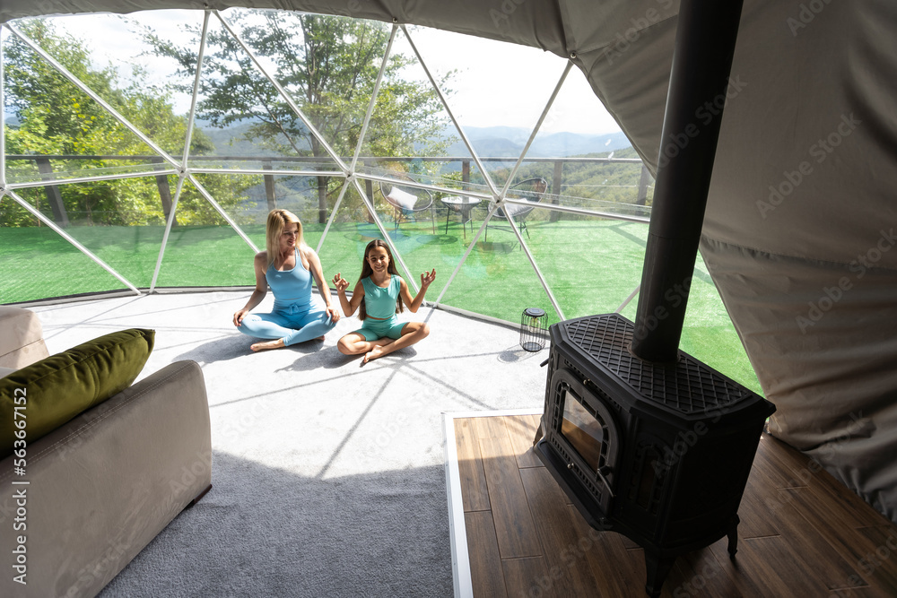 mother and daughter doing yoga and meditation indoor in a glamping dome tent