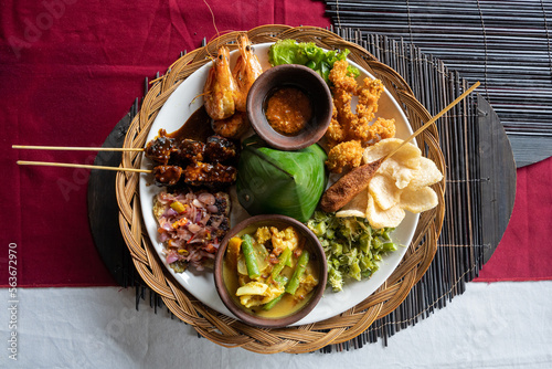 A plate of Indonesian Nasi campur (Indonesian for mixed rice) with seafood on a table at a restaurant