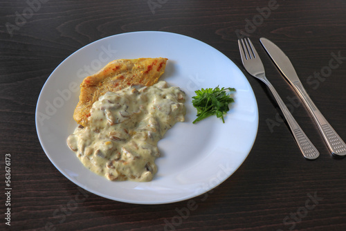 Plate of grilled chicken with mushroom sauce on wooden background.