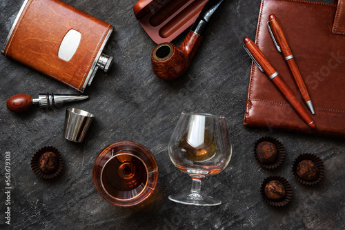 Glass of brandy or cognac and accessories on dark table, flat lay