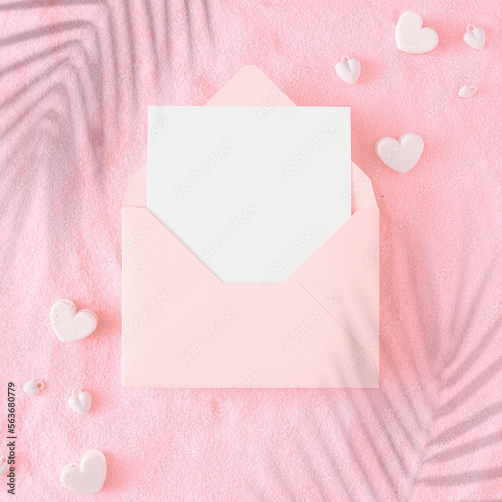 Valentines Day concept. Flat lay photo of open envelope with white card, hearts baubles and tropical leaf shadows on pink sandy background. Wedding or honeymoon idea. Valentines Day concept. Flat lay photo of open envelope with white card, hearts baubles and tropical leaf shadows on pink sandy background. Wedding or honeymoon idea.