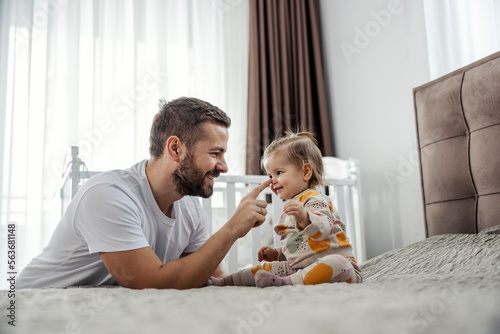 A little girl is sitting on a bed in a bedroom while her father booping her nose.
