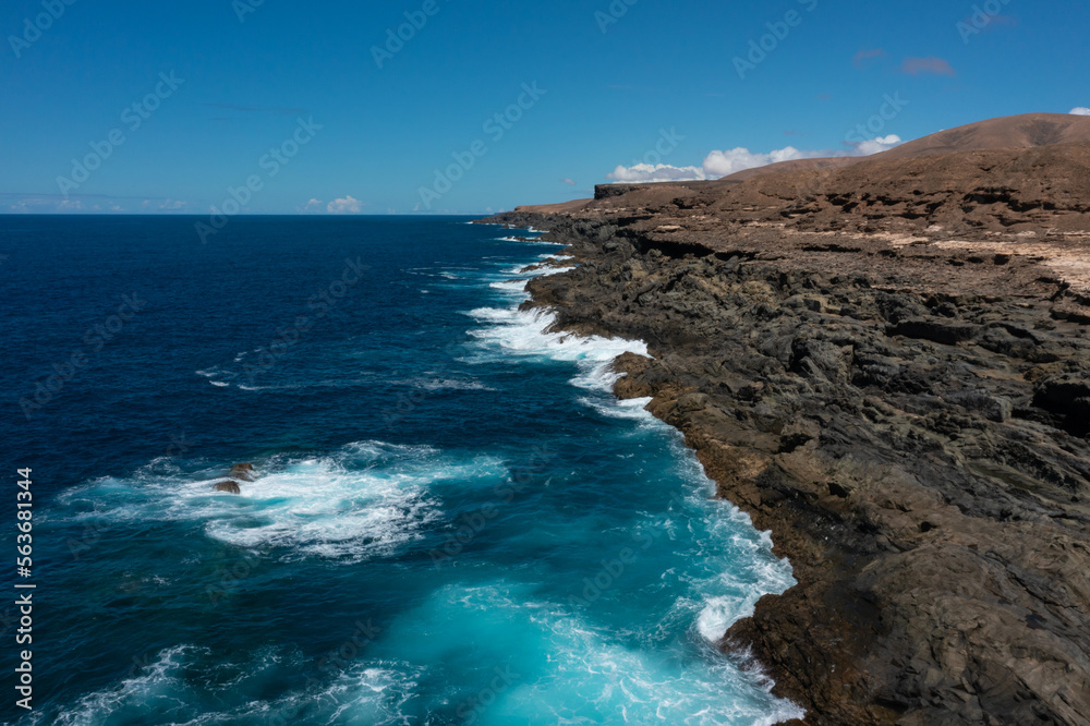 Obraz premium Beautiful landscape with deep blue water. Powerful waves crash against black volcanic rocks on the coast of ´Aguas Verdes, Fuerteventura island. Selective focus, blurred background.
