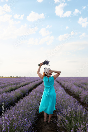Rear view of woman in hat holding a bouquet of lavender flowers on the field