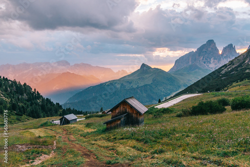 Traditional wooden houses in the Italian Alps in a cinematic landscape with golden light  a mountain road and impressive mountains. Dolomites  Italy. Popular travel destination. Summer tourism.