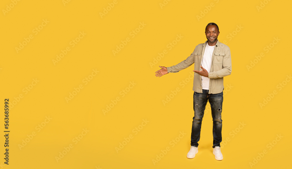 Cheerful middle aged african american male in casual showing hands on copy space, recommends ad and offer