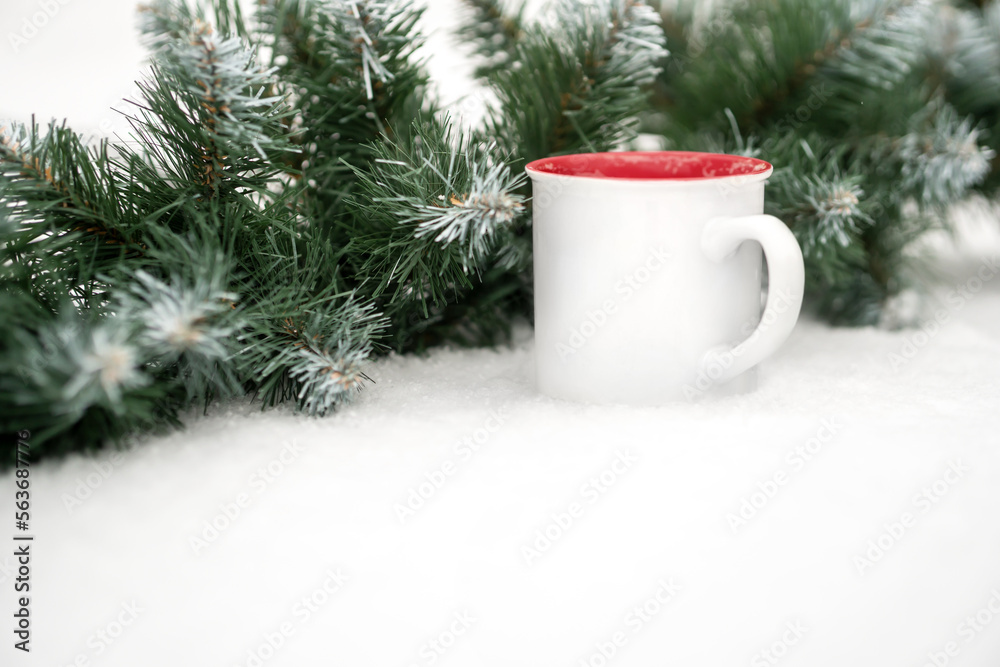 a mug of coffee on the snow near a coniferous garland. a mug of coffee on the snow near a coniferous garland.