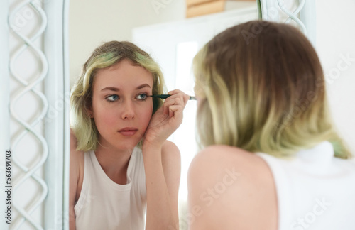 Teenage girl doing makeup with black eyeliner.