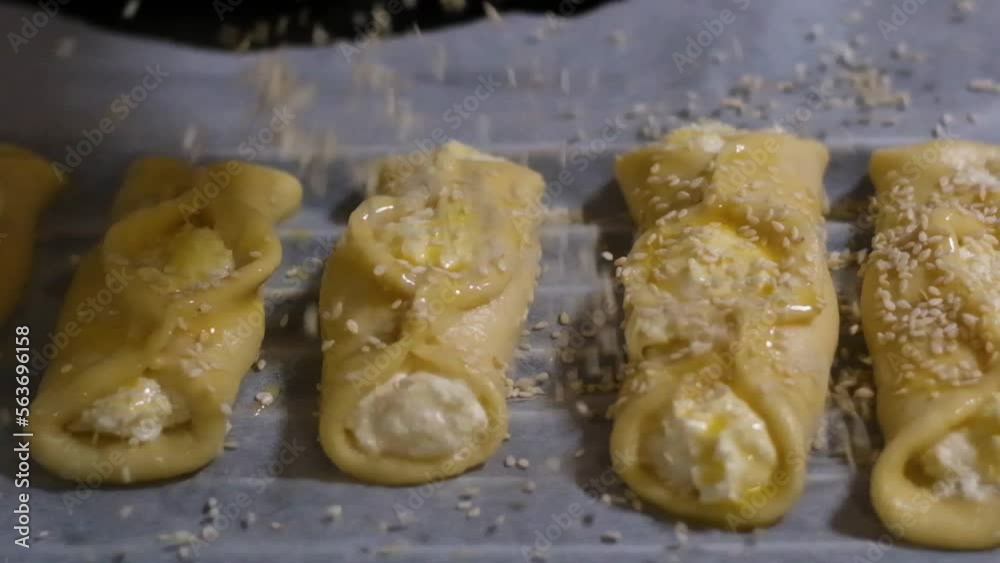 cakes on a baking sheet sprinkled with sesame seeds slow motion cooking delicious food raw yeast dough and curd filling smeared with egg coming off the dough waiting to put in the oven cakes on a baking sheet sprinkled with sesame seeds slow motion cooking delicious food raw yeast dough and curd filling smeared with egg coming off the dough waiting to put in the oven