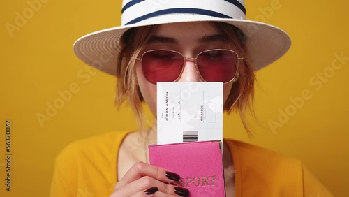 Vacation planning. Conspirator woman. Boarding pass. Pretty lady in summer look looking from foreign passport with tickets posing yellow background. photo