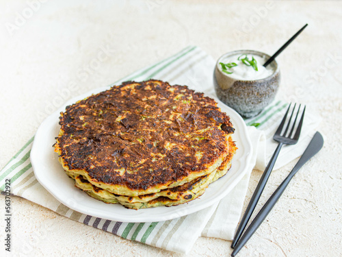 Vegetarian food - zucchini fritters on white background with sour cream sauce in a ceramic gravy boat. Close up, copy space. Healthy food. Breakfast.