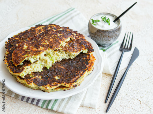 Vegetarian food - zucchini fritters on white background with sour cream sauce in a ceramic gravy boat. Close up, copy space. Healthy food. Breakfast.