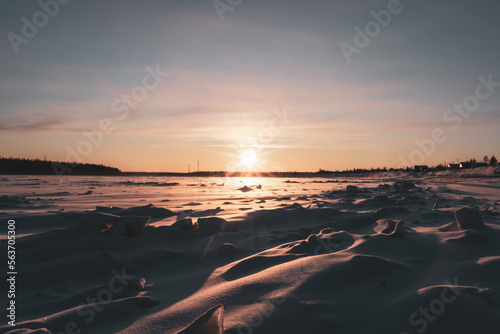 The bright winter sun sets over the forest on the horizon, casting rays on the protruding ice floes on the Vilyui River in Yakutia. photo