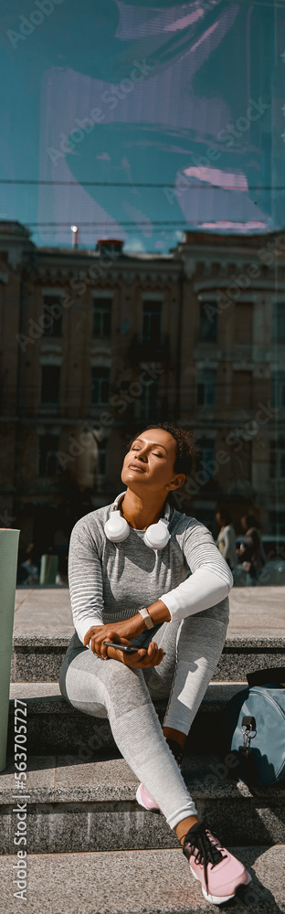 Slim woman dressed in active wear resting in urban setting. People and sport concept