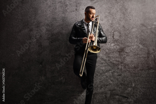 Canvas Print Young man holding a trombone and standing against a wall