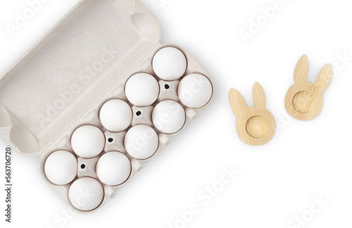 ten white chicken eggs in a cardboard box and an egg stand in the form of a rabbit on a white background