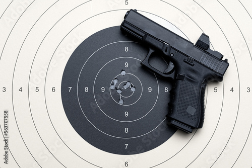 A target for shooting with bullet holes in the center and a pistol with a red dot sight. photo